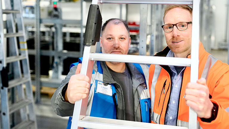 Schichtleiter Christian Appel und Thomas Menke, Leiter Operations Kommissionierung, schauen durch eine Leiter.