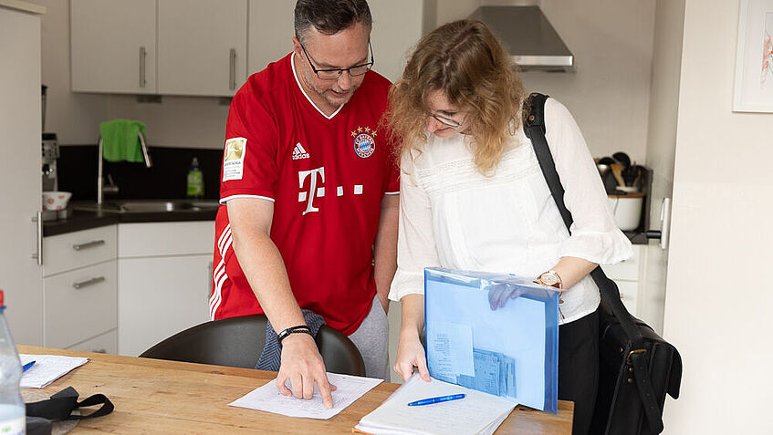 Steven Wedhorn und Sarah Baugärtner stehen in der Küche und schauen auf den Therapieplan, der auf dem Tisch liegt.