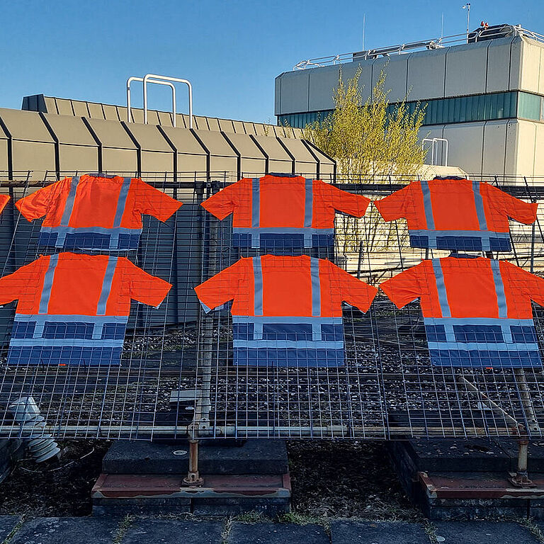 Auf einem Büroflachdach sind zehn orangefarbene Warnwesten auf einem Gitter ausgebreitet.
