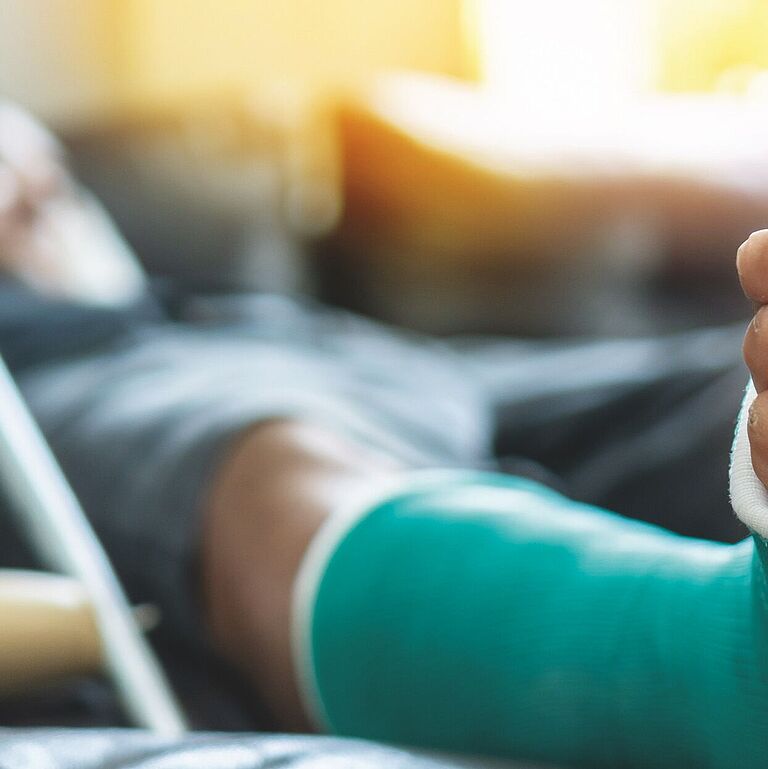 Eingegipster Fuß mit Gehhilfe im Hintergrund