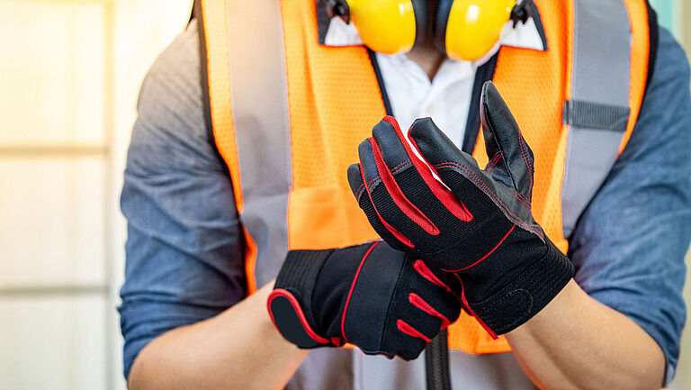 Person mit oranger Warnweste zieht schwarze Schutzhandschuhe an