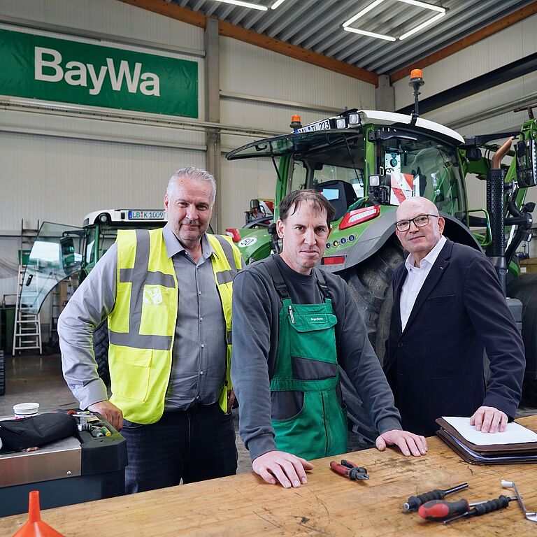 Drei Männer stehen in einer Werkshalle.