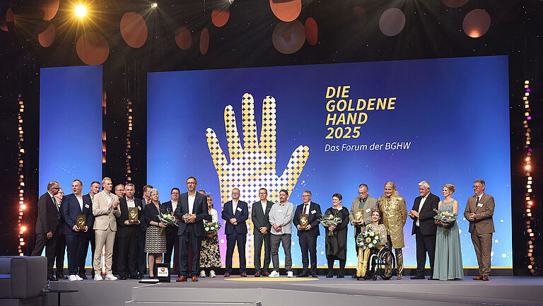 Preisverleihung DIE GOLDENE HAND 2025 in Mannheim. Die Preisträger stehen gemeinsam auf der Bühne. Die Moderatoren im Vordergrund.