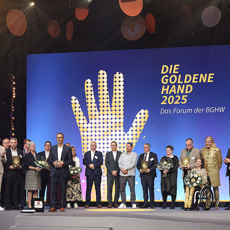 Preisverleihung DIE GOLDENE HAND 2025 in Mannheim. Die Preisträger stehen gemeinsam auf der Bühne. Die Moderatoren im Vordergrund.