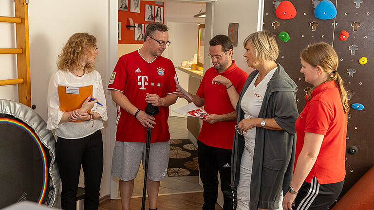Sarah Baumgärtner, Steven Wedhorn und das Team der Praxis "Physiologisch" stehen in einem Trainingsraum zusammen und besprechen Stevens Therapieplan. 
