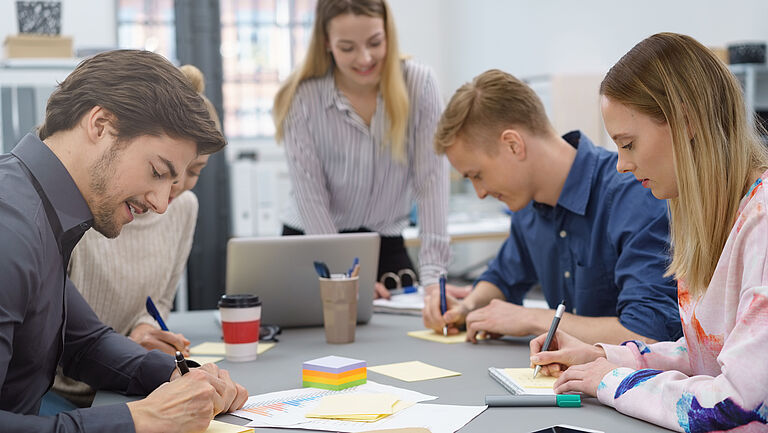 Eine Gruppe junger Menschen sitzt an einem Meetingtisch beim Brainstorming