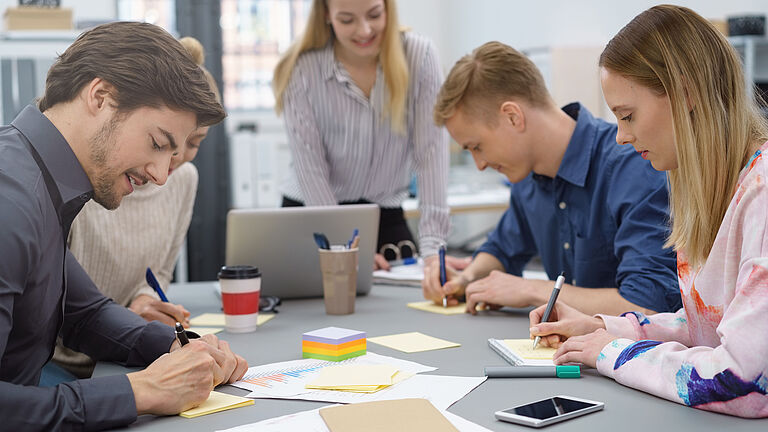 Eine Gruppe junger Menschen sitzt an einem Meetingtisch beim Brainstorming