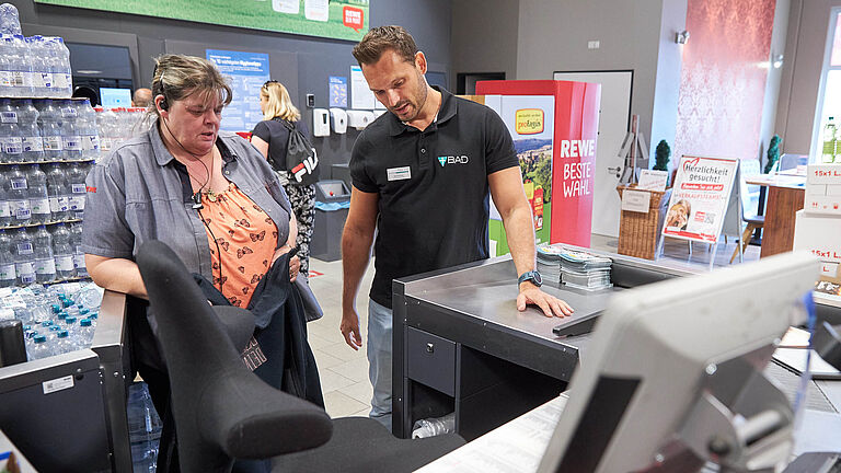 Ergonomie-Trainer berät Supermarktangestellte an der Kasse