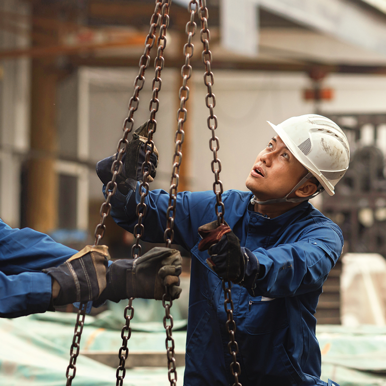 In einer Produktionshalle bewegen zwei asiatische Arbeiter eine Last.