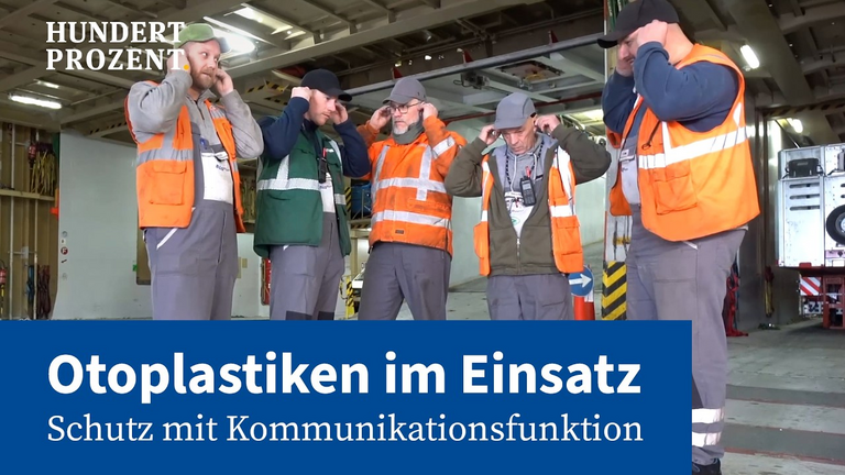 Fünf Hafenarbeiter stehen nebeneinander im Frachtschiff und stecken sich ihren Gehörschutz in die Ohren.