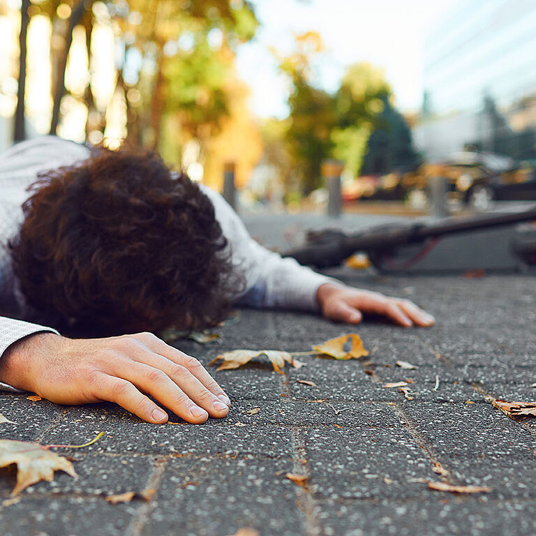 Eine Person liegt mit dem Gesicht auf dem Asphalt, im Hintergrund liegt ein E-Scooter