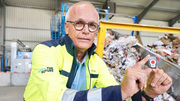 Andreas Sirries, H & S Manager bei Smurfit Kappa Recycling und Fachkraft für Arbeitssicherheit, hockt neben dem Förderband und hält eine Transponderuhr in den Händen. 