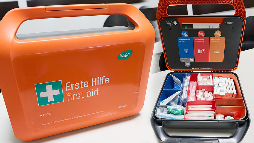 Moderner orangefarbener Erste-Hilfe-Koffer, einmal geschlossen, einmal geöffnet mit Sicht auf die Inhalte des Koffers.