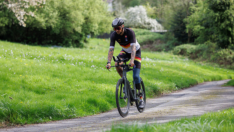 Paratriathlet Kim Cremer fährt mit dem Rennrad durchs Grüne.