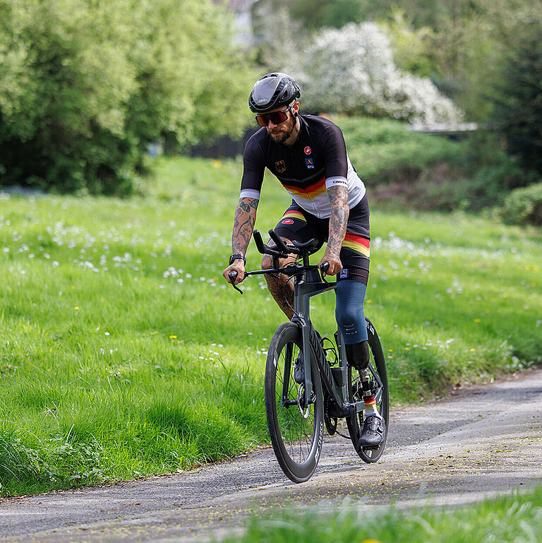 Paratriathlet Kim Cremer fährt mit dem Rennrad durchs Grüne.