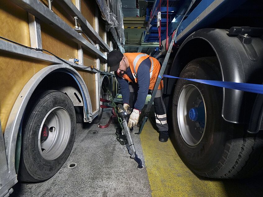 Hafenarbeiter sichert die Ladung mit schweren Ketten zwischen Fahrzeugen an Deck eines Frachtschiffs.