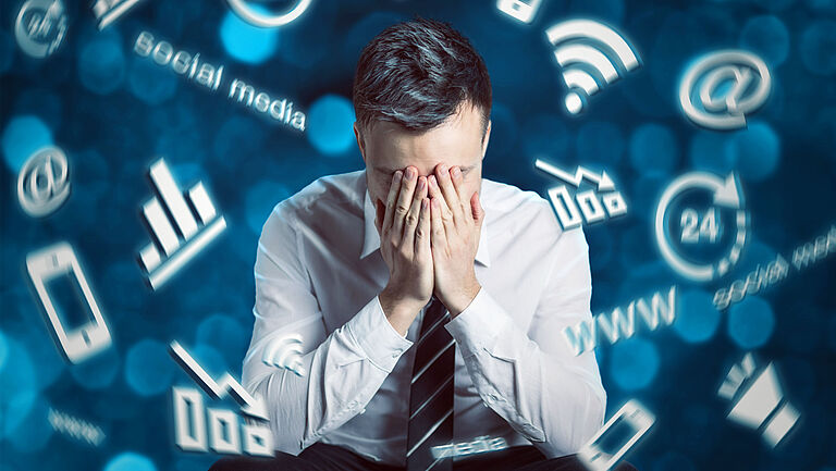 Mann mit Krawatte hält sich die Hände vor das Gesicht, weil er mit der digitalen Welt überfordert ist. Digitale Symbole schwirren um seinen Kopf herum.