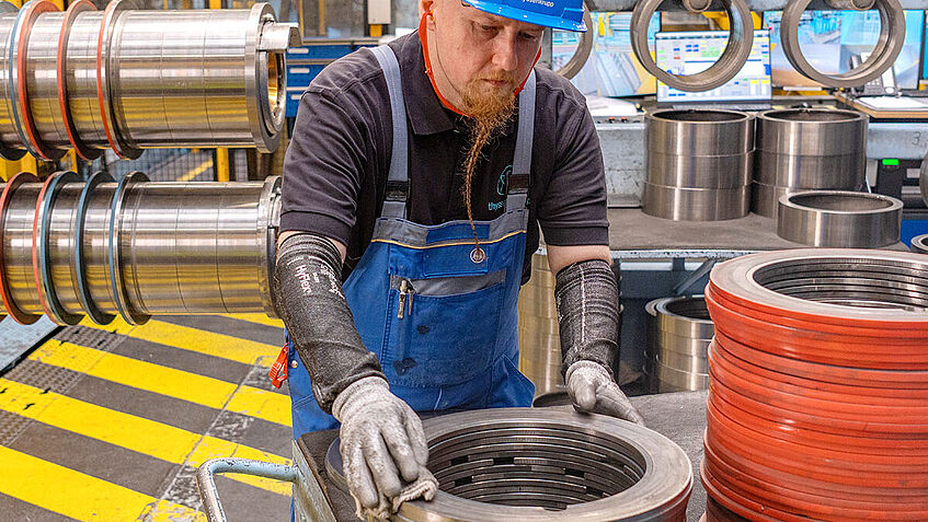 Mitarbeiter mit Schutzhelm in der Stahlverarbeitung prüft mit Schutzhandschuhen Material.