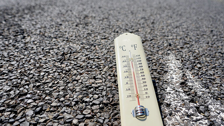 Das Bild zeigt ein Thermometer mit 40-Grad-Anzeige, das auf dem Asphalt liegt.