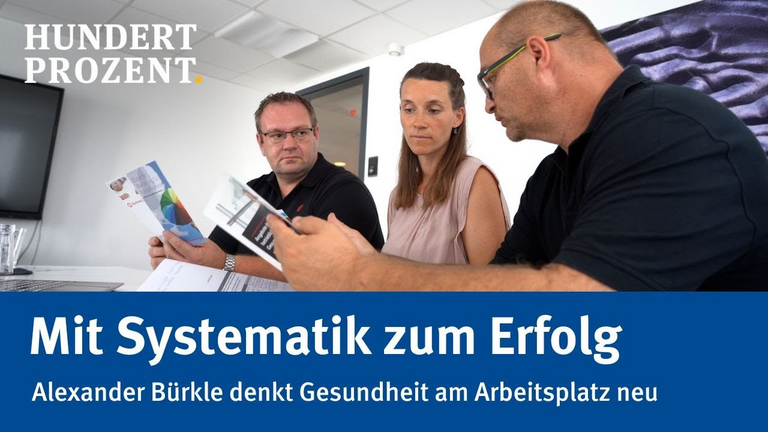 Zwei Männer und eine Frau sitzen an einem Tisch und schauen sich Broschüren an