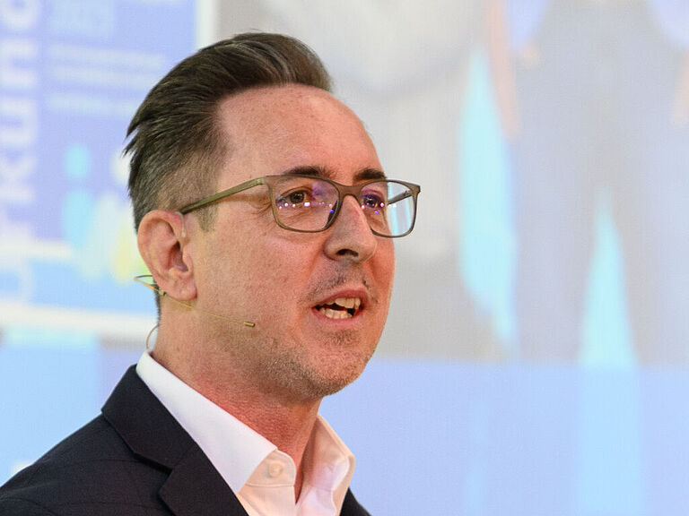 Sven Königer, Leiter der BGHW-Stabsstelle Rehabilitation und Leistung, steht an einem Stehtisch und erklärt gestikulierend konkrete Schritte