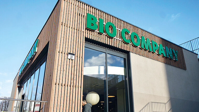 Verputzte Außenfassade mit Holzverkleidung der Filiale Yorckstraße mit gläsernen Eingangstüren sowie grünem Logo der Bio Company