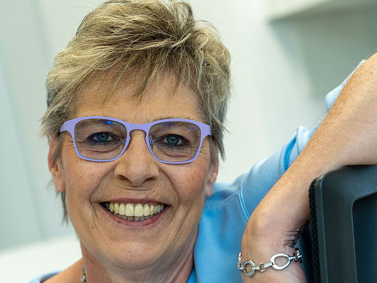 Ute Grötzinger lehnt sich an das Rückenteil ihres Bürostuhls und hat die Arme über die Lehne gelegt. Sie lächelt in die Kamera. 