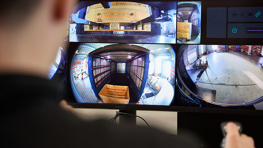 Das Bild zeigt einen Remote-Fahrer, der auf den Monitor blickt, um einen fahrerlosen Gabelstapler zu steuern.