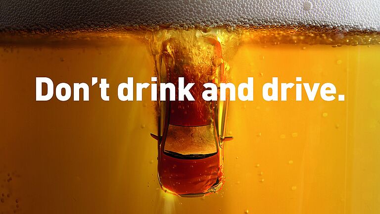 Ein Auto taucht senkrecht in ein Glas mit schäumendem, hellen Bier ein.