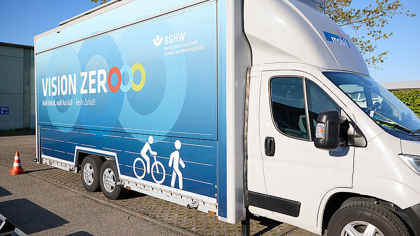 Das BGHW mobil, ein Klein-Lkw, mit geschlossener Seitenfläche. Auf der Seitenfläche stehen Vision Zero und das Logo der BGHW