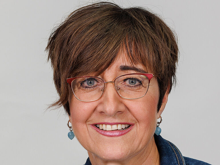 Ein Porträtfoto; Eine Frau mit braunen kurzen Haaren schaut freundlich in die Kamera. Sie trägt eine Jeansjacke und ein weißes T-Shirt. 