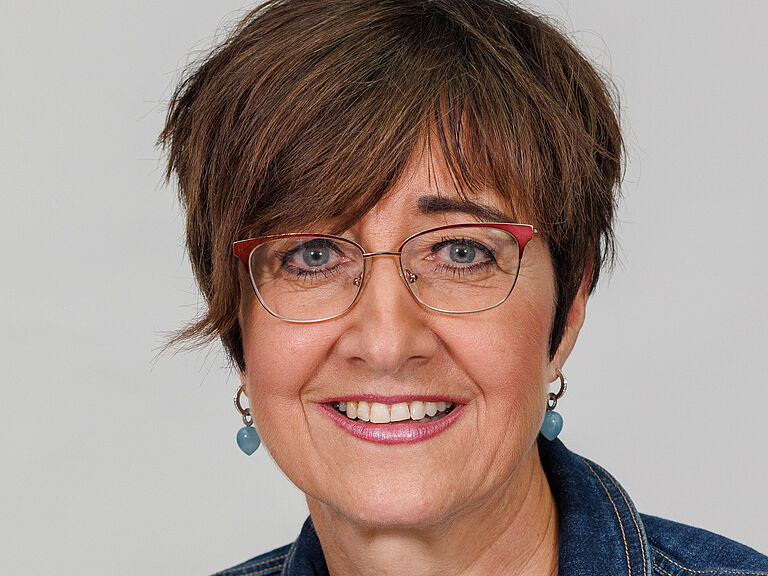 Ein Porträtfoto; Eine Frau mit braunen kurzen Haaren schaut freundlich in die Kamera. Sie trägt eine Jeansjacke und ein weißes T-Shirt. 