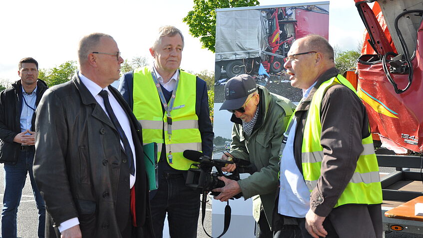 Verkehrssicherheitsaktion: drei Männer im Gespräch vor dem Exponat LKW Kabine. Ein vierter Mann filmt mit der Kamera.