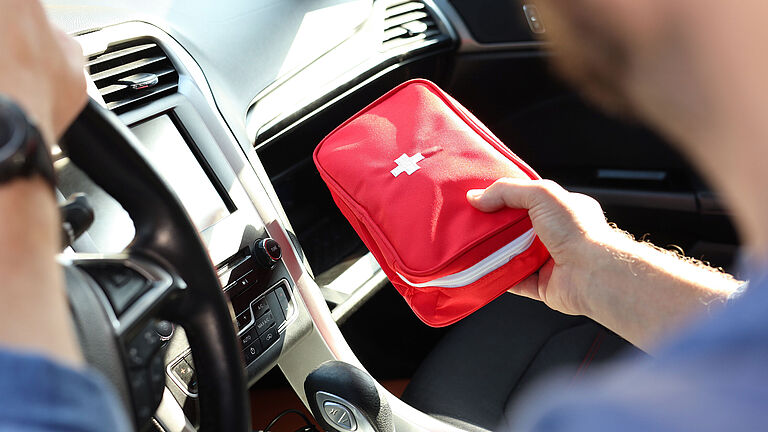 Das Bild zeigt einen Kfz-Verbandkasten, der aus einem Handschuhfach geholt wird.