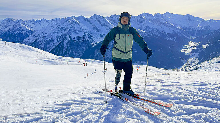 Theo Müller seht in Wintersportkleidung auf Skiern im Schnee, im Hintergrund ein Bergpanorama.