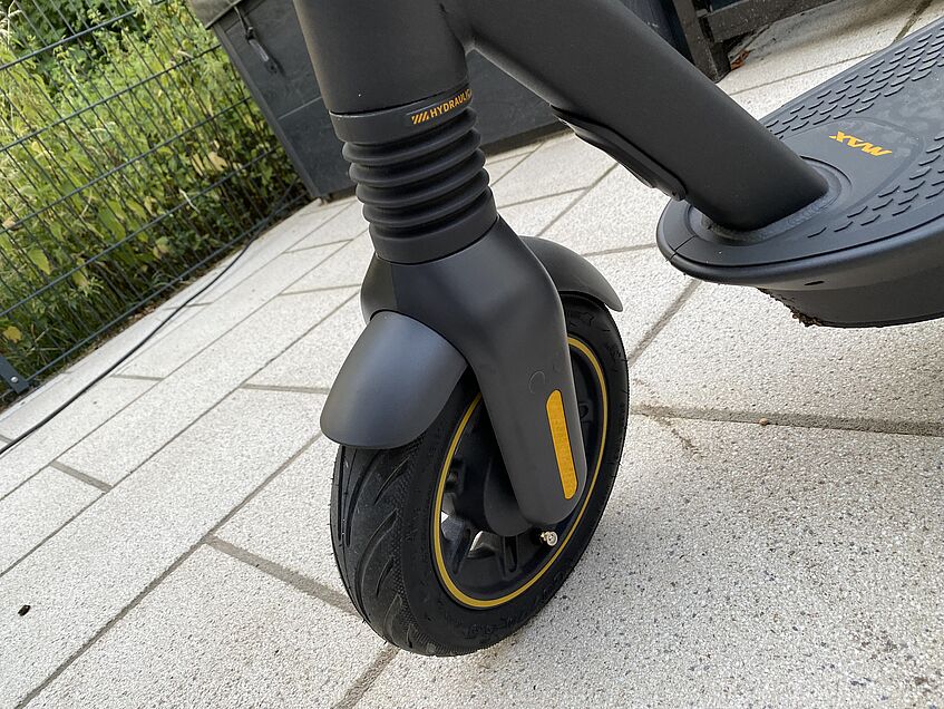 Vorderrad und Gabel eines schwarzen E-Scooters mit Dämpfung steht auf Pflaster.