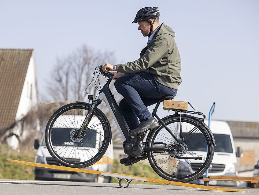 Das Bild zeigt einen Teilnehmenden beim Fahrsicherheitstraining, der auf seinem Pedelec über ein Kippelbrett fährt.