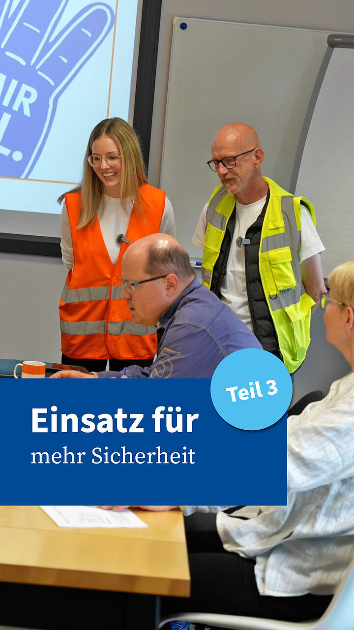 Mehrere Teilnehmende einer Besprechung sitzen an einem Konferenztisch, während zwei Personen in Warnwesten stehend mit ihnen sprechen. Im Bild eingeblendet ist der Text „Einsatz für mehr Sicherheit – Teil 3“. Mehrere Teilnehmende einer Besprechung sitzen an einem Konferenztisch, während zwei Personen in Warnwesten stehend mit ihnen sprechen. Im Bild eingeblendet ist der Text „Einsatz für mehr Sicherheit – Teil 3“.