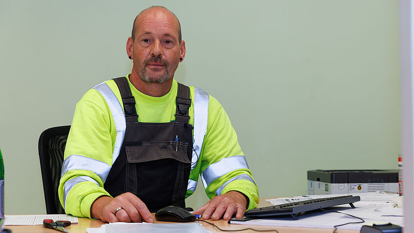 Dirk Boßmeyer an seinem Schreibtisch sitzt an seinem Schreibtisch. Vor ihm liegen Unterlagen und Papiere.