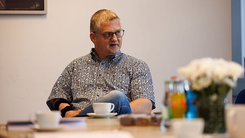 Thorsten Hammerich, Essmann-Standortleiter in Wattenbek, sitzt an einem Tisch mit Kaffeetassen und Blumen und schaut zur Seite! 