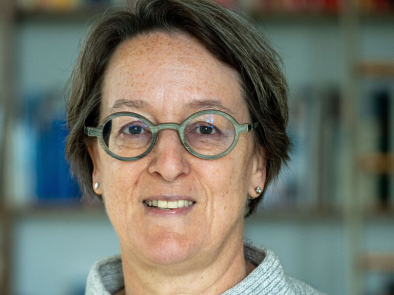 Porträtaufnahme von Professor Kathrin Yen. Sie stehr vor einem Bücherregal, das leicht unscharf im Hintergrund zu sehen und schaut freundlich in die Kamera. 