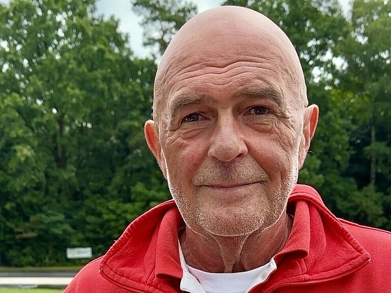 Ein Mann mit Glatze, im roten Pullover, schaut freundlich in die Kamera. 