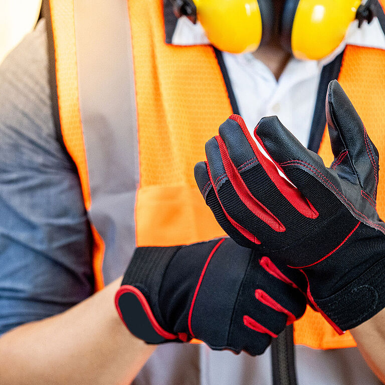 Person mit oranger Warnweste zieht schwarze Schutzhandschuhe an