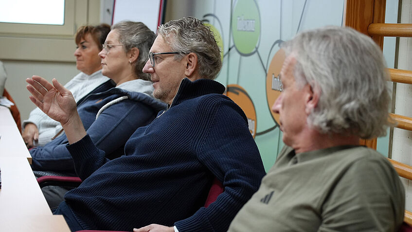 Angehende Sportcoaches sitzen im Seminarraum. Andreas, zweiter von rechts, spricht gestikulierend. 