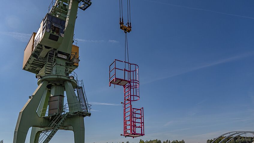 Ein Kran hebt eine mobile Leiterkonstruktion hoch.
