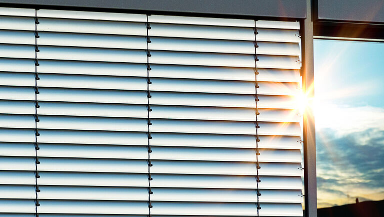 Ein Fenster mit einer Außenjalousie, dazu Sonnenstrahlen