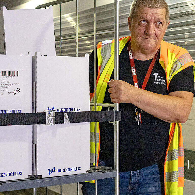 Ein Mann schiebt einen Rollcontainer, der mit dem neuen Gummispanngurt fixiert ist, seitlich neben sich her.