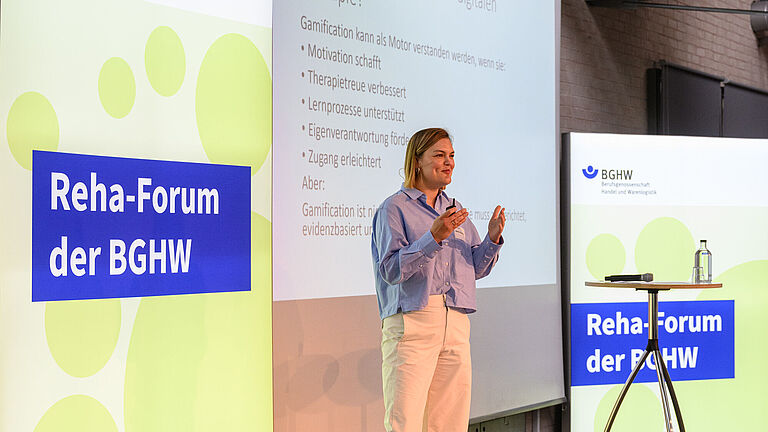 Maike Schrader, Gesamtleiterin Therapie des BG Klinikums Duisburg, steht gestikulierend auf der Bühne des Reha-Forums und spricht in ein Mikrofon. 