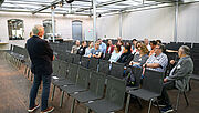 Das Bild zeigt einen Workshop während des Reha-Forums: Links steht der Referent, im zugewandt sitzen auf den Stühlen des Veranstaltungsraums rund 15 Teilnehmende und tauschen sich zum Thema Reha-Management aus. 