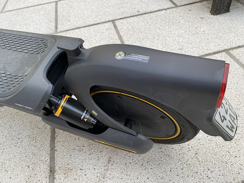Hinterrad und Federung eines schwarzen E-Scooters mit Hinterraddämpfung und Kennzeichen.